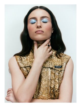 Madeline Argy poses with eyes closed wearing gold Miu Miu dress.