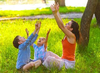 Mom, daughter and son sitting in the outdoors at a picnic meditate stretching out their hands to the sun at sunset 