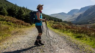 A woman stands on a rocky hill path, holding trekking poles and wearing Salewa Ortles Ascent Mid Gore-Tex Boots.