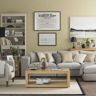 neutral living room with prints on the wall, a light grey chaise sofa with cushions, matching armchair, light grey display cabinet and wooden rectangular cubed coffee table