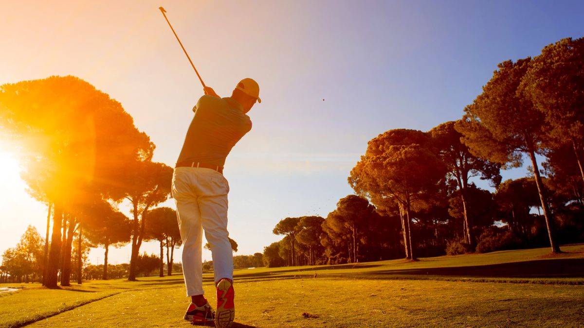 A golfer teeing off with the sun low in the sky in the background