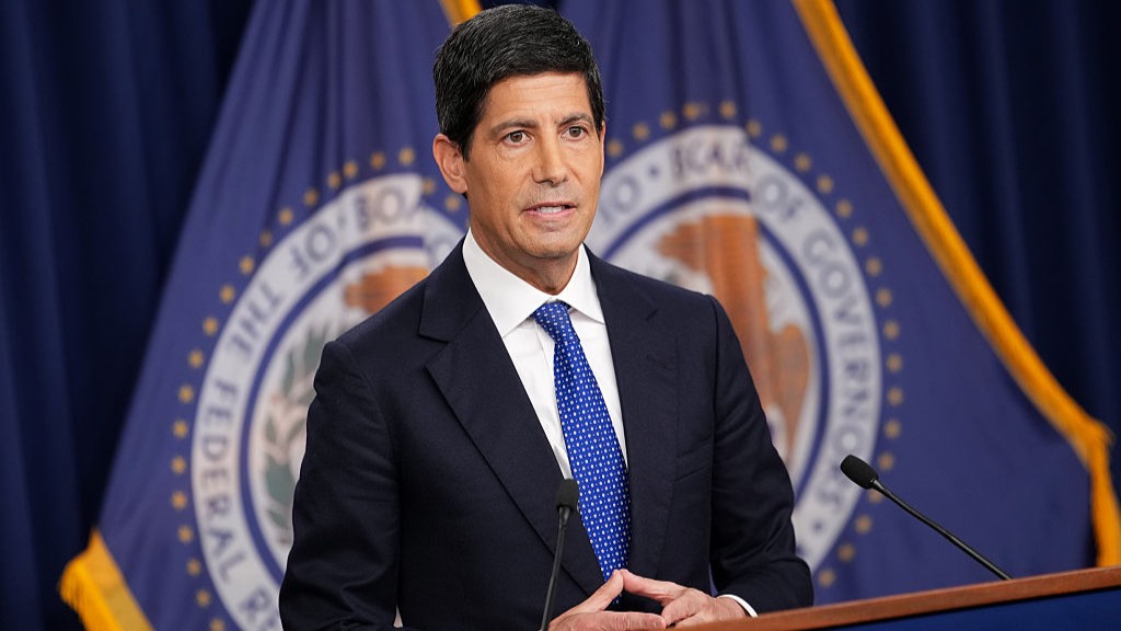 Federal Reserve Chair Kevin Warsh stands at a podium with two Fed flags behind him