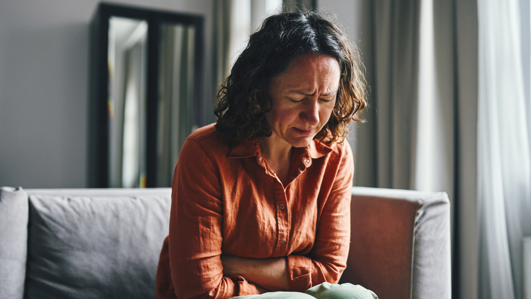 A woman sits on the sofa with her arms folded over her stomach