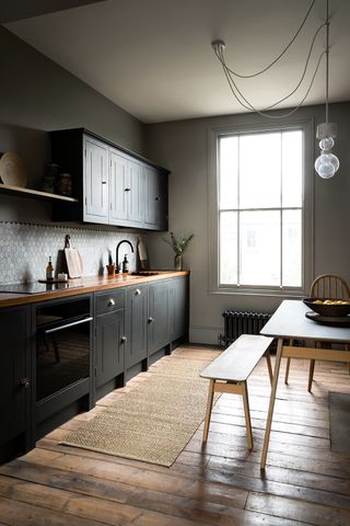 Black kitchen in a small apartment with warm wooden details and a wooden bench