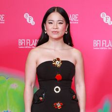Kelly Marie Tran wears a black strapless gown with gold metal floral embellishments down the center. 