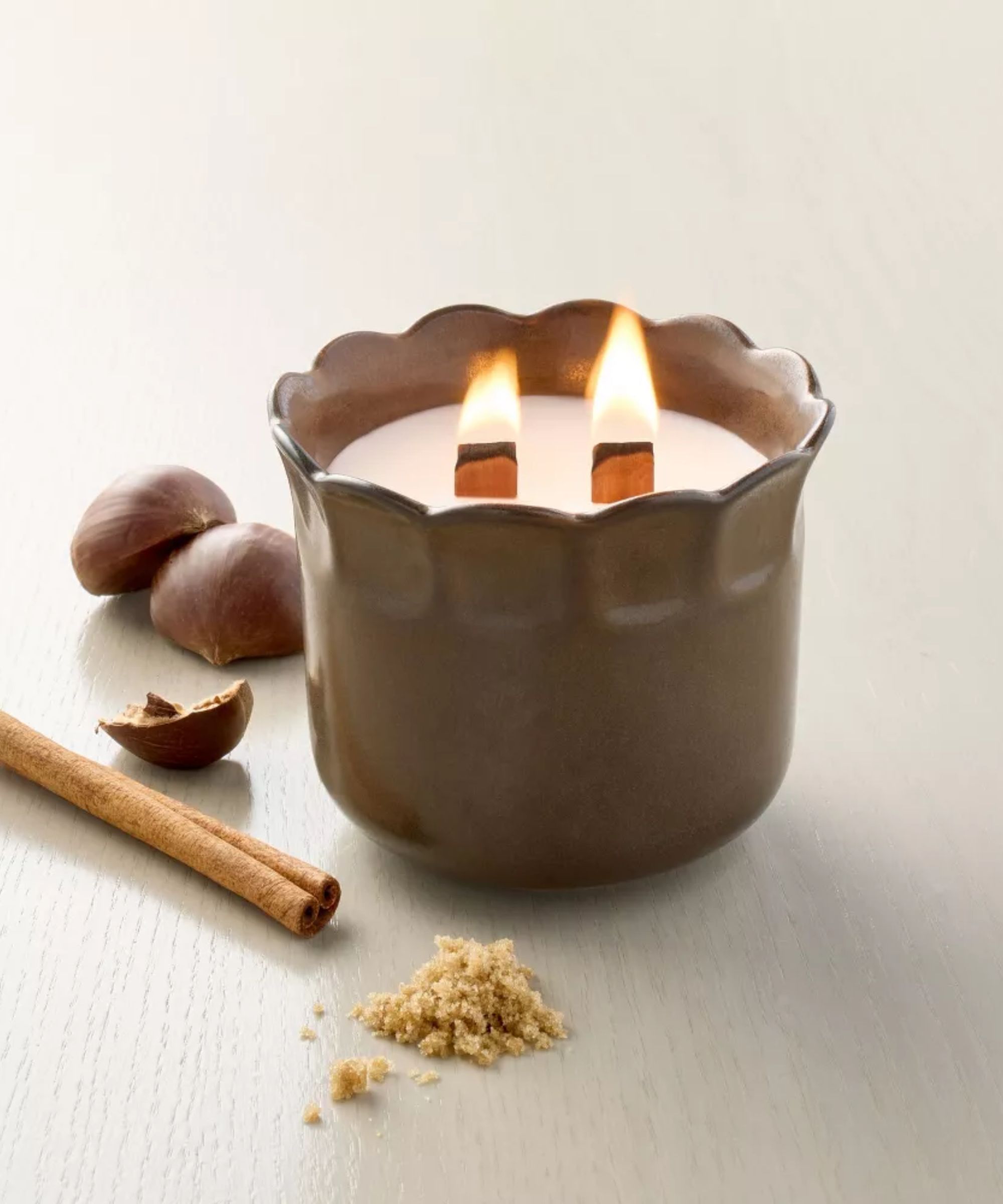 Brown scalloped candle on a wooden table next to halved chestnuts and a cinnamon stick