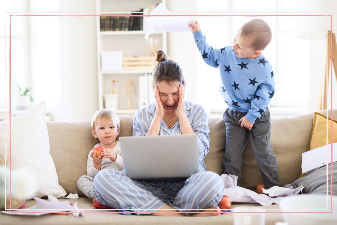 A sat on a sofa with her head in her hands while two children play next to her