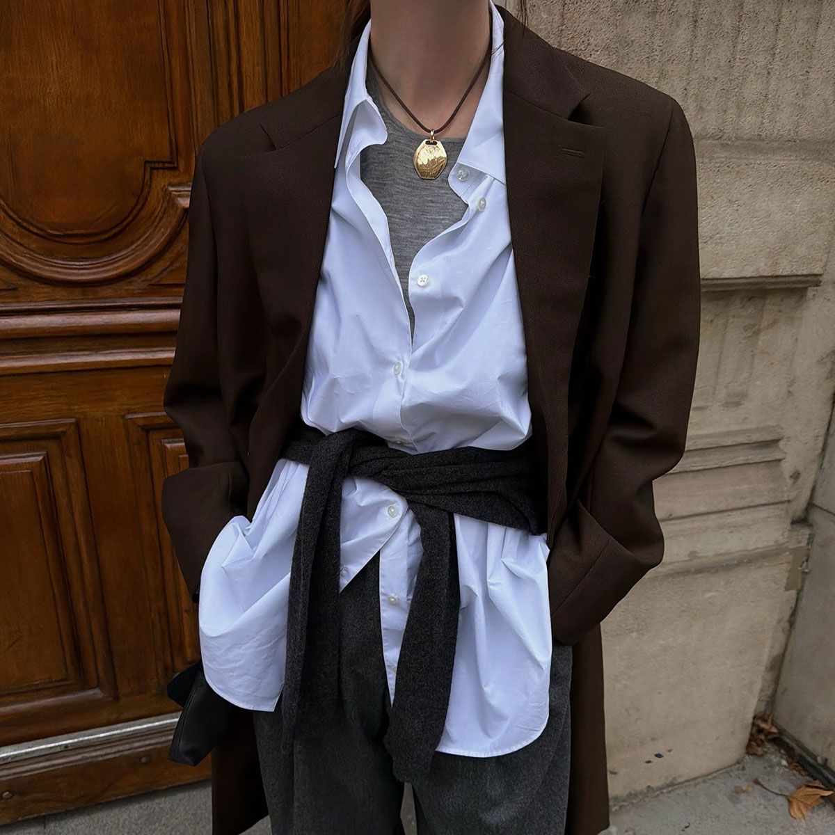 @annabelrosendahl casual outfit closeup in white button down, brown blazer, gold necklace, and sweaters under and around waist 