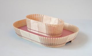 Wooden waste paper bin and desk tray in the shape of a boat photographed against a grey background