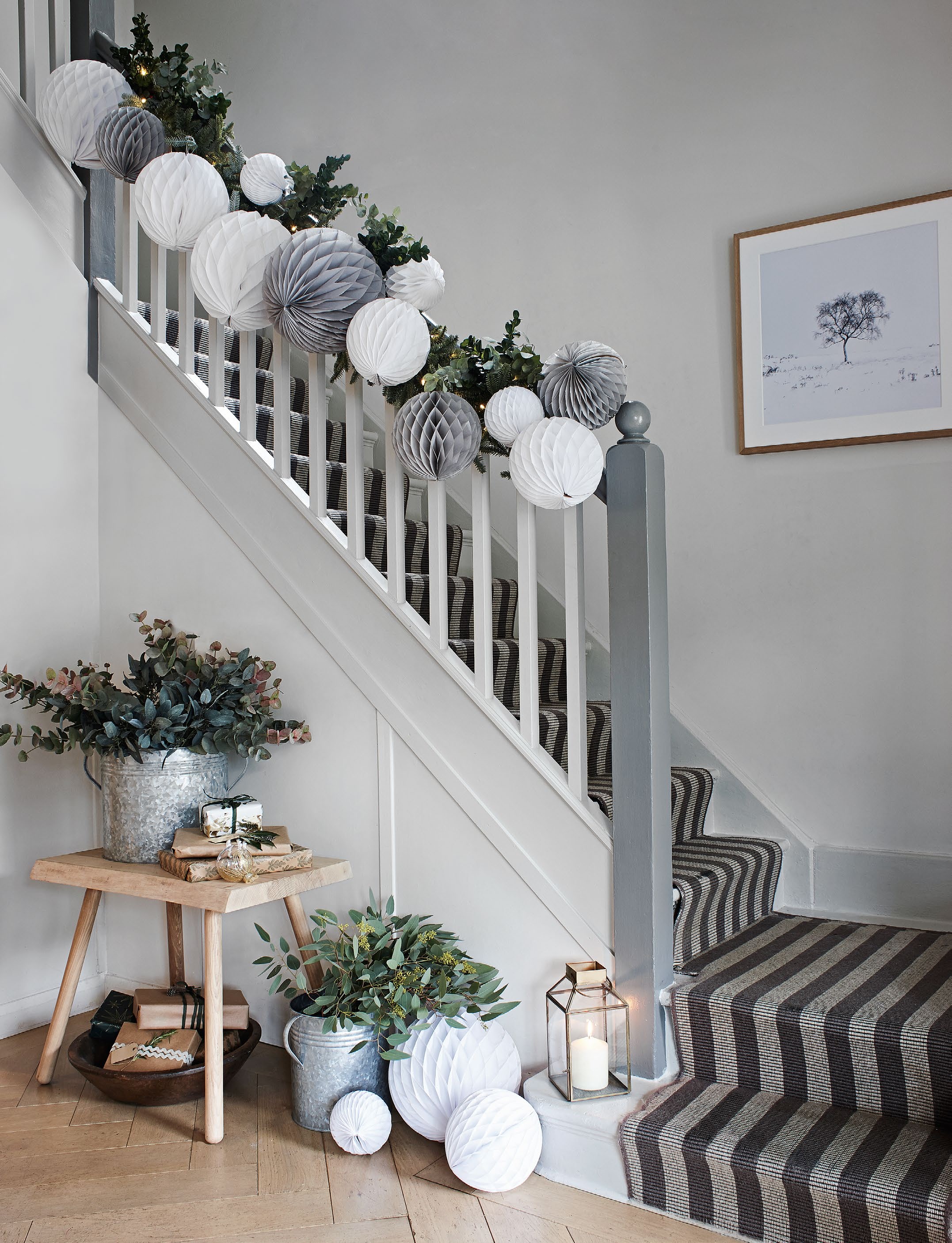 A stylish staircase decorated with a garland of concertina-style paper balls in white, gray, and green, accompanied by potted plants and a lantern.