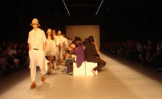 Models in white outfits walk down one side of the runway