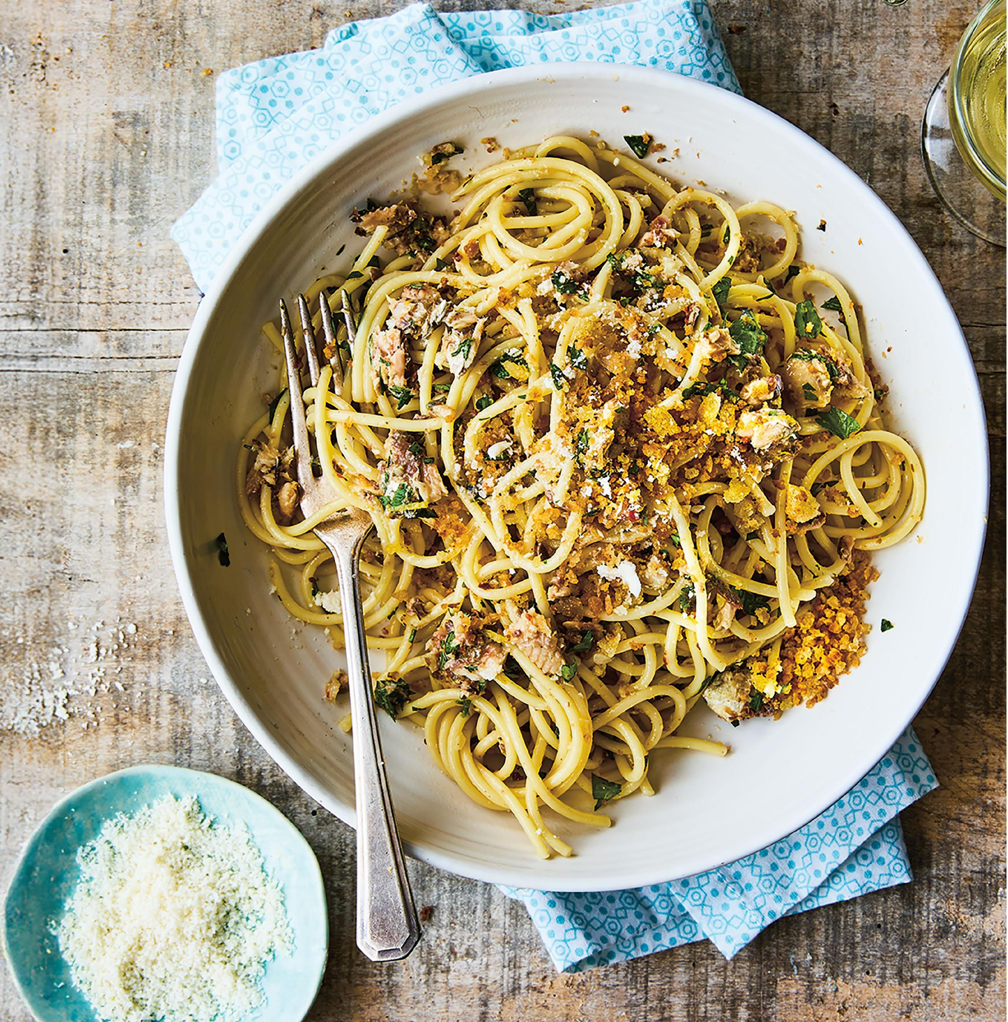 A plate of sardine spaghetti with a plate of Parmesan to the side