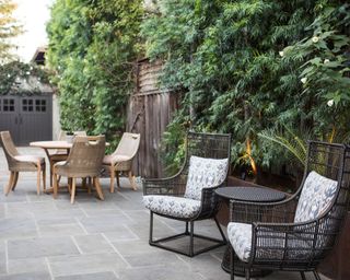 A long paved patio garden with a selection of wicker seating and climbing plants, demonstrating small back yard landscaping ideas.