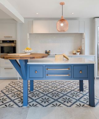 Blue kitchen island zoned with patterned blue and white floor tiles in rug effect.
