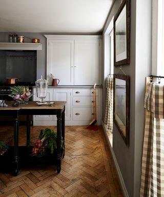 Small open plan kitchen ideas illustrated in a pale gray scheme with herringbone wooden flooring and check drapes.