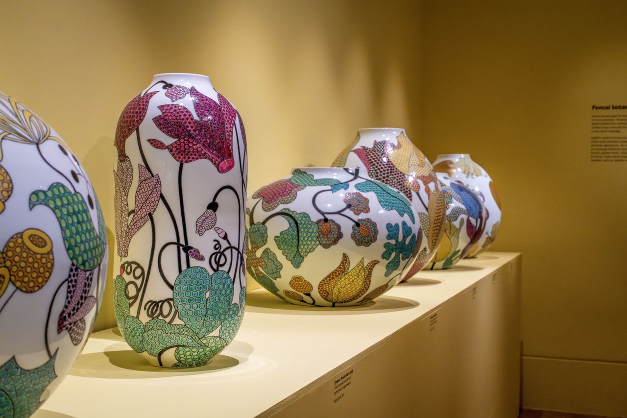 A series of gigantic china-style vases is on display in a warmly lit gallery, including some blue and white pieces and some more widely colored ones.
