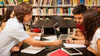 Teens studying with laptop and tablet computer in library.