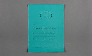 View of ﻿Hermès' bluey green leather invitation pictured against a grey background