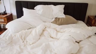 An unmade bed with a big white down duvet over the top and lots of pillows