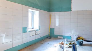 Large empty room with green plasterboard on walls, covered with large format white tiles