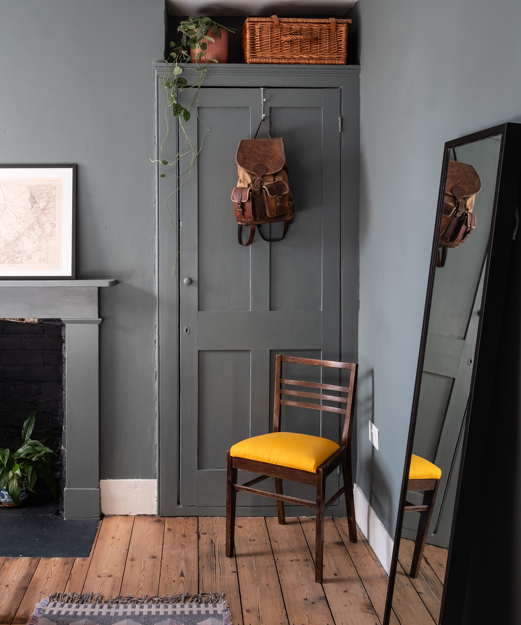 A bedroom with wooden flooring and grey-painted walls. There is a cupboard built into an alcove with a yellow chair in front