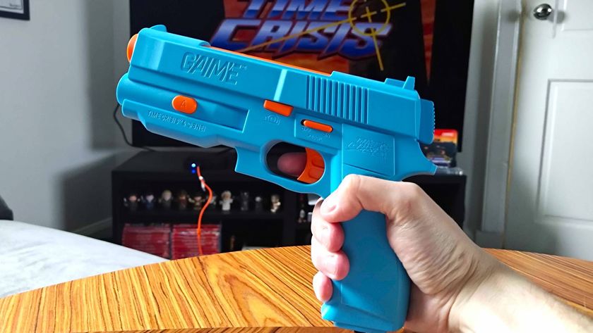 Hand holding G&#039;AIM&#039;E Time Crisis Lightgun connected to console with TV running game in backdrop.