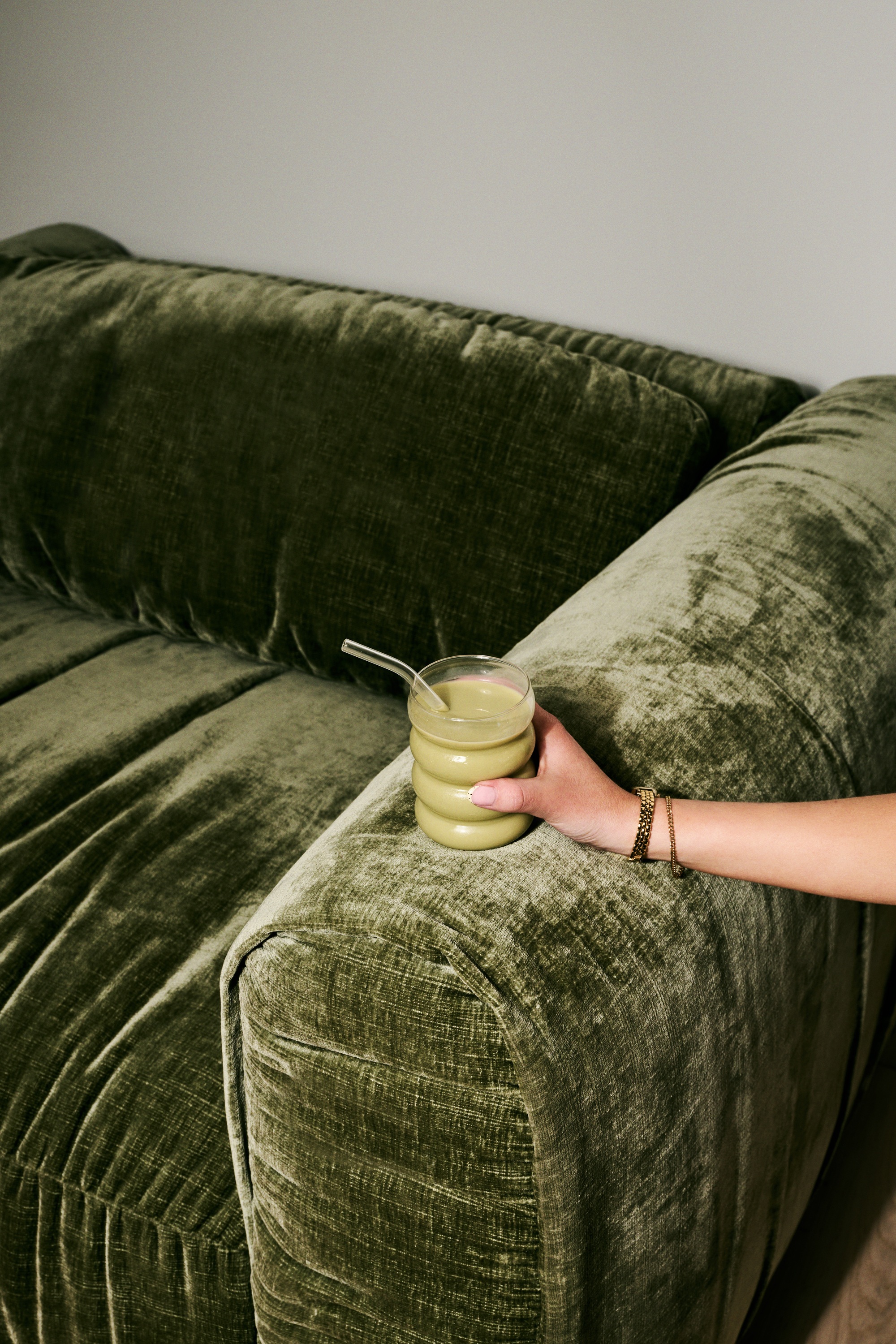A hand holding a matcha over a green velvet sofa.