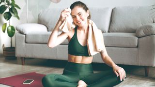 a photo of a woman in workout wear wiping her face with a towel and smiling