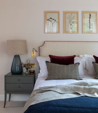 neutral bedroom with linen upholstered headboard, dark blue throw and gray bedside chest