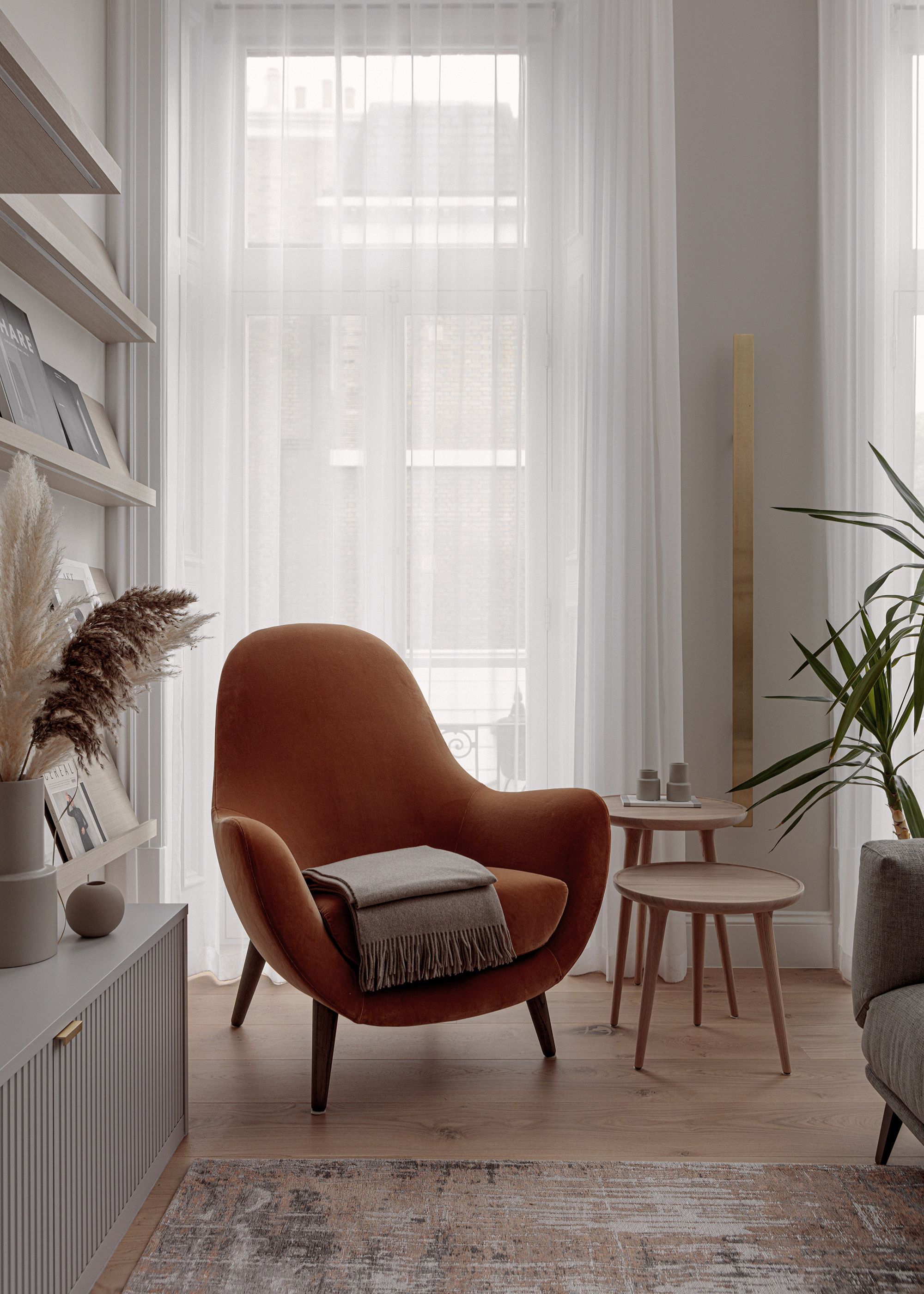 corner of room with neutral walls, large window with voile curtains, burnt orange armchair