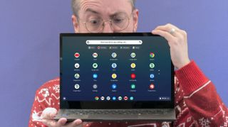 A person with glasses holds a laptop displaying a colorful app interface against a purple background. They appear surprised or intrigued.