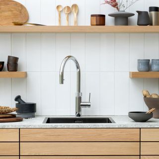 Silver instant boiling water tap on white kitchen countertop with wooden cabinets