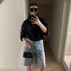 Woman wears cotton shirt, blue denim shorts and carries black bag