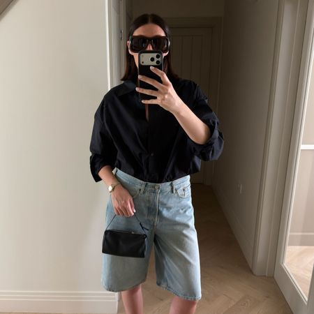 Woman wears cotton shirt, blue denim shorts and carries black bag