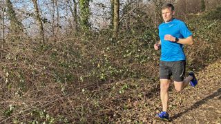 Trail runner wearing Inov8 TrailTalon all-terrain running shoes on gentle downhill slope in winter