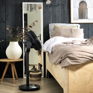 Black fan on floor next to bed with linen sheets