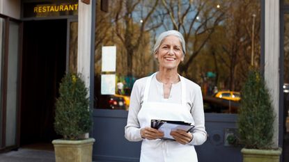 mature woman small business owner outside her restaurant with menus
