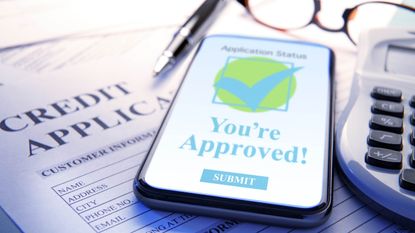 A mobile device indicating that credit approval has been granted rests on top of a credit approval. A ballpoint pen, a calculator, and a pair of eyeglasses rest next to the device. Photographed with a very shallow depth of field.