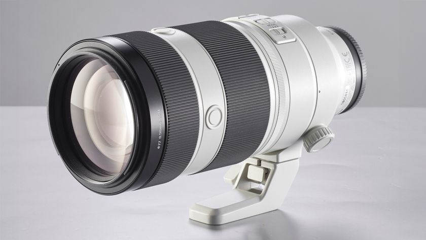 A sleek, silver-and-black camera lens rests on a light surface, featuring a tripod mount and textured grip sections for stability and control