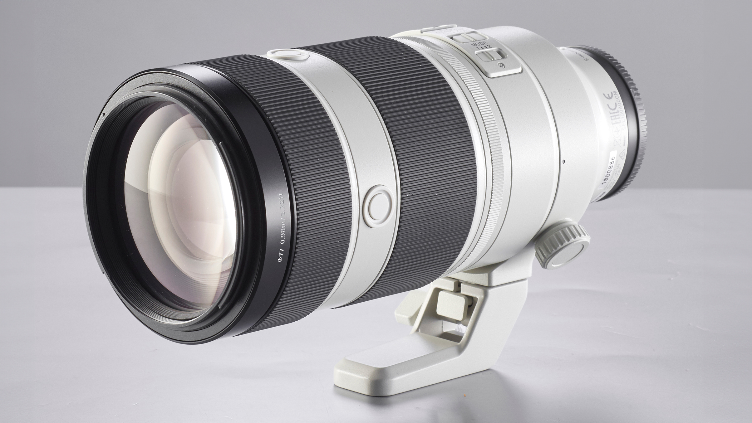 A sleek, silver-and-black camera lens rests on a light surface, featuring a tripod mount and textured grip sections for stability and control