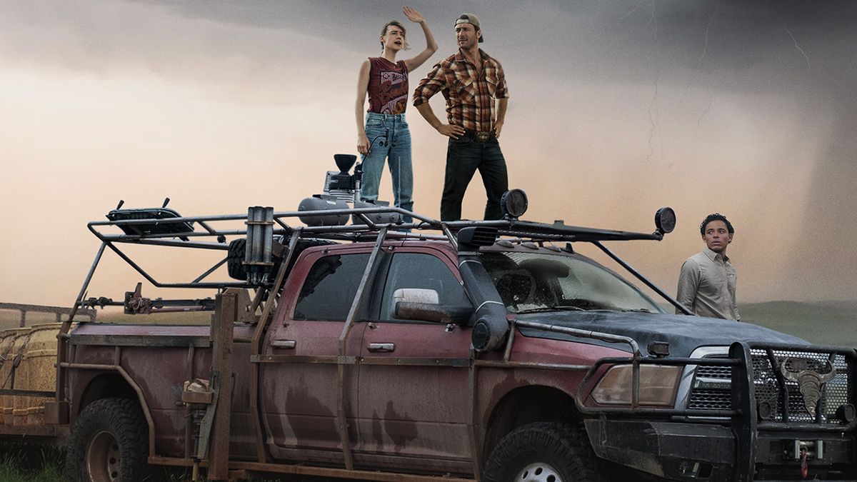 Glen Powell, Daisy Edgar-Jones And Anthony Ramos looking at a tornado from a car in the official Twisters poster.