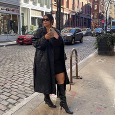 gia wears black leather trench, black mini dress, and black long heeled boots on the streets of NYC