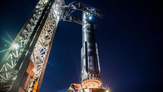 a silver spacex starship rocket is lowered onto its launch mount at night