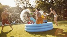 A family playing on a backyard lawn, with kids in a paddling pool