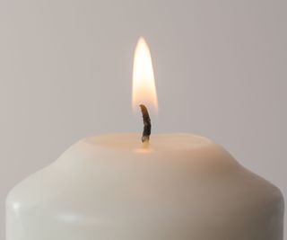 A candle wick on a pale candle in front of a white wall