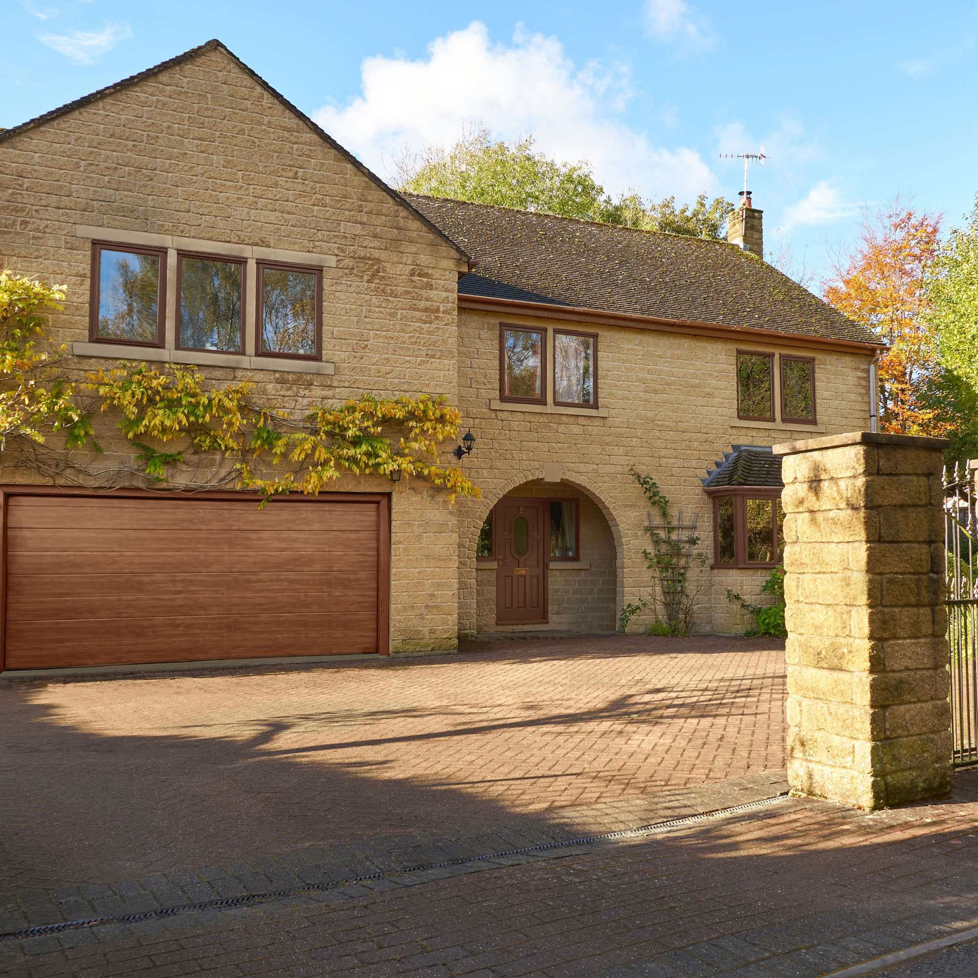 buff stone house with arched porch and wooden garage door in driveway with dropped kerb