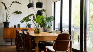 Open plan dining area of a home near doors to a patio with houseplants on the table and sideboard