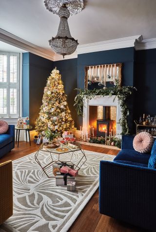 A blue living room with a Christmas tree and fireplace with wood burner decorated with a garland