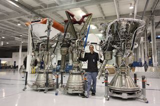 a man stands in a hangar between two cone-shaped rocket engines