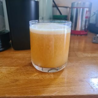 glass of fresh apple carrot and ginger juice on a wooden kitchen counter in front of a Philips Viva Cold Press Masticating Slow Juicer